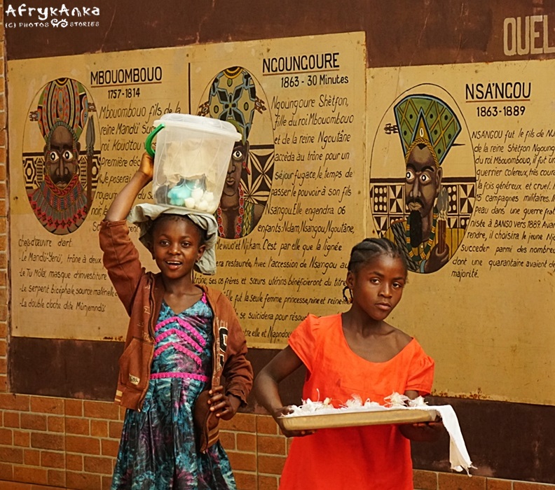 Ddiewczynki przy wejściu do pałacu, w tle portret królowej Ngungure.